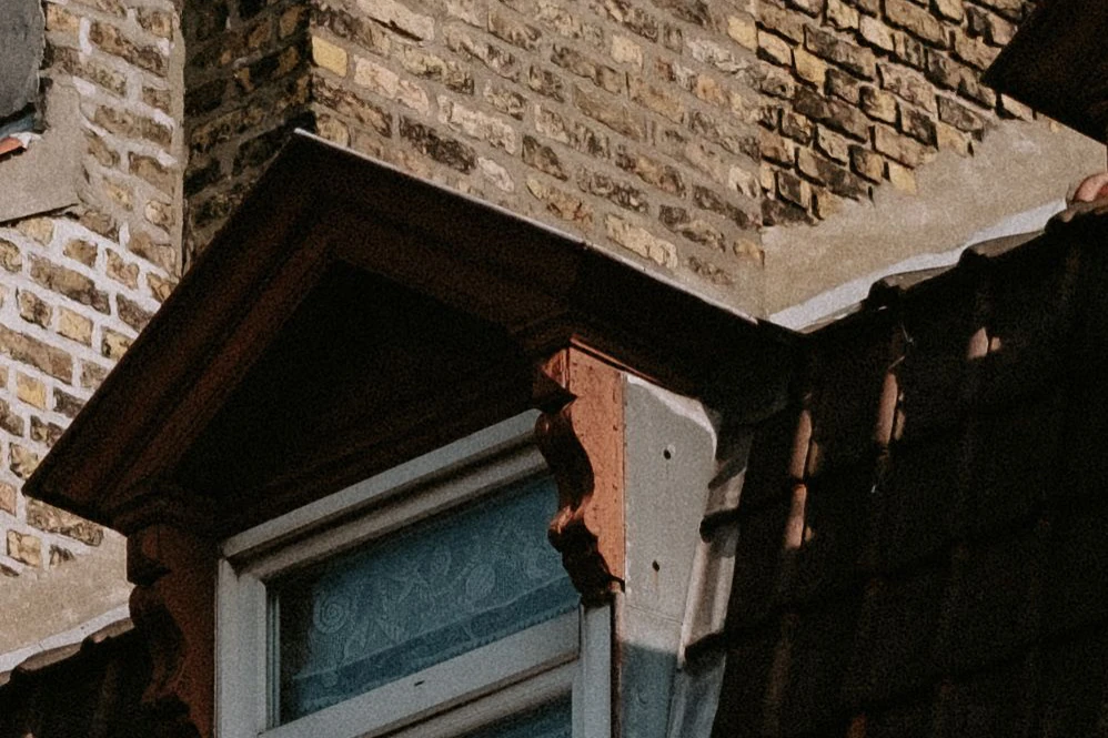 Crop of a dormer window with a lace curtain and brickwork, original